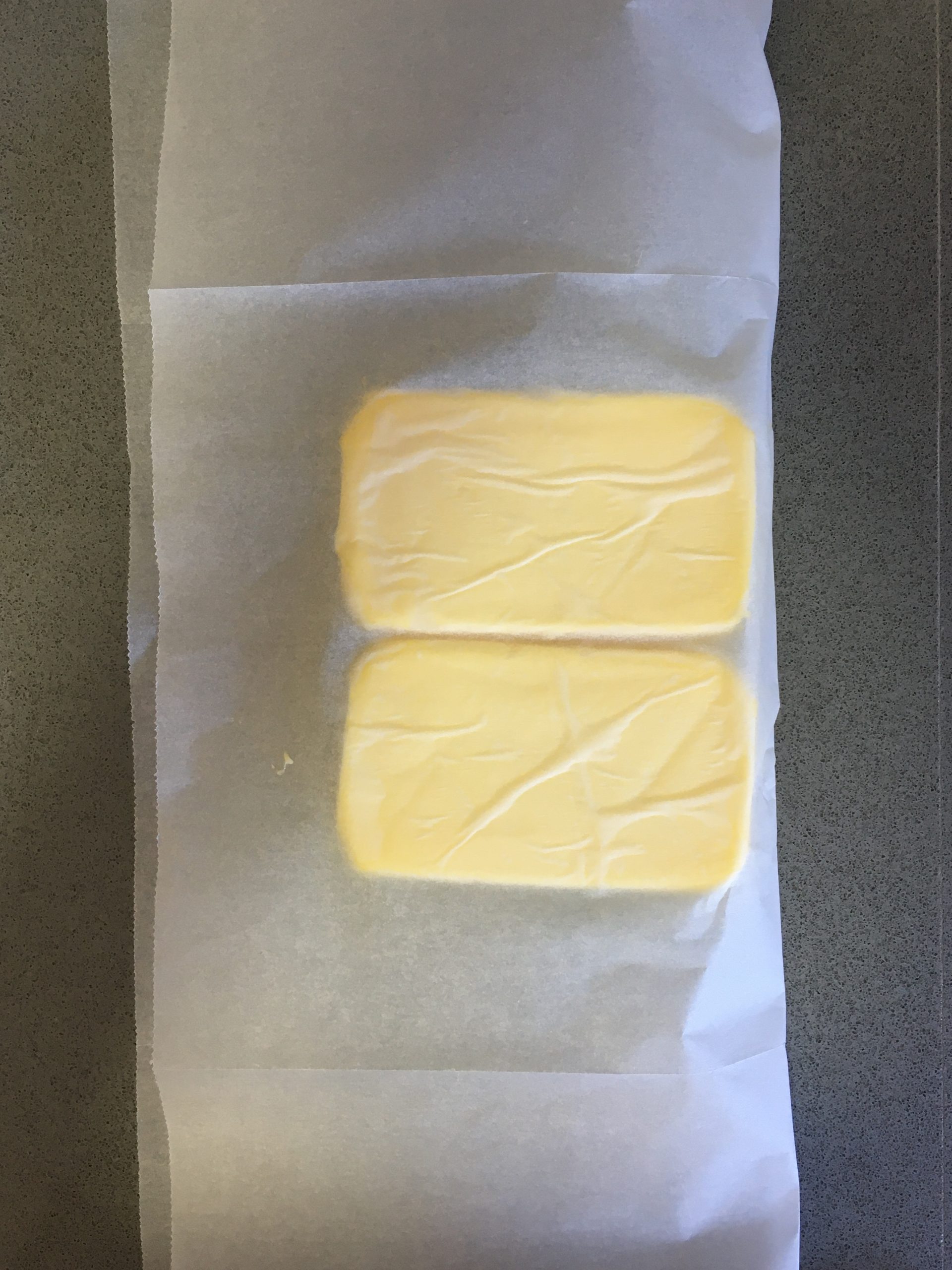 פורסים נייר אפייה ומניחים על מחצית ממנו את בלוק החמאה. מקפלים את צידו השני כך שיכסה את החמאה.